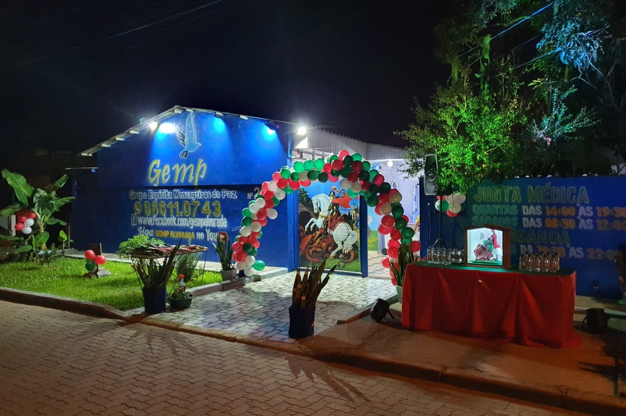 Sede do GEMP iluminada em noite de festa, com arco de balões e fachada azul